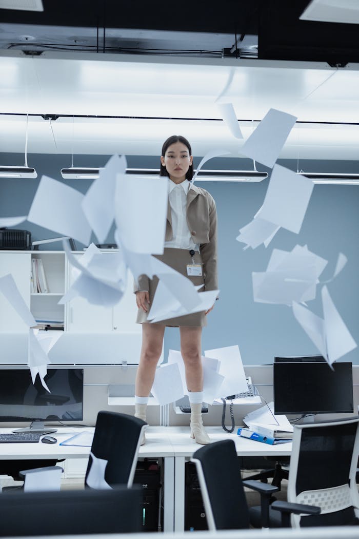 A woman in a modern office with papers flying around, capturing a dynamic and energetic moment.